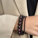 Essential Garnet bracelet stacked with the Petite and Chunky Garnet bracelets on a wrist with a beige blazer