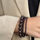Petite Garnet bracelet worn as part of a three-bracelet garnet stack, styled with a beige blazer