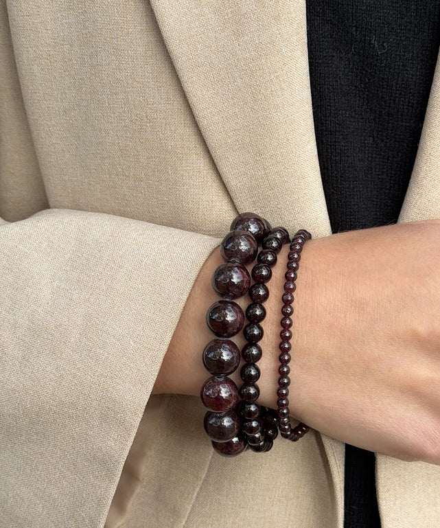 Petite Garnet bracelet worn as part of a three-bracelet garnet stack, styled with a beige blazer