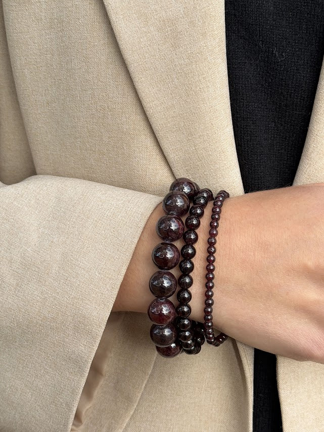 Petite Garnet bracelet worn as part of a three-bracelet garnet stack, styled with a beige blazer