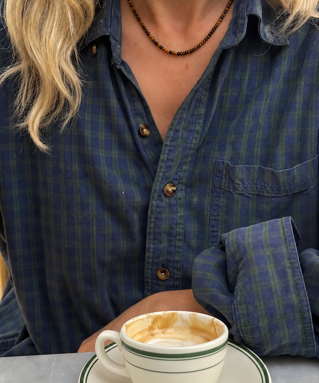 Luna Tiger Eye halskæde båret til en blåternet skjorte ved en kop kaffe